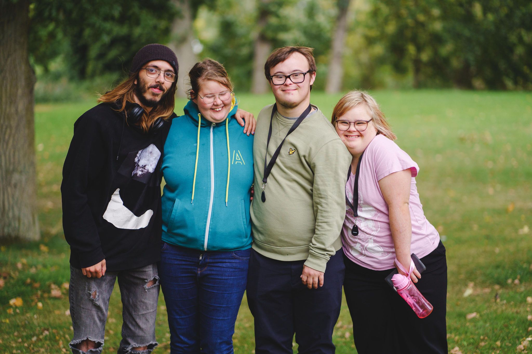 Fyra deltagare står utomhus, håller om varandra och ler in i kameran. 