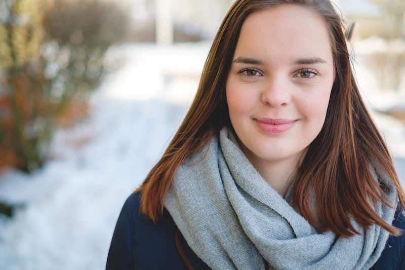 En bild på Agnes, hon står utomhus en solig vinterdag och ler mot kameran.