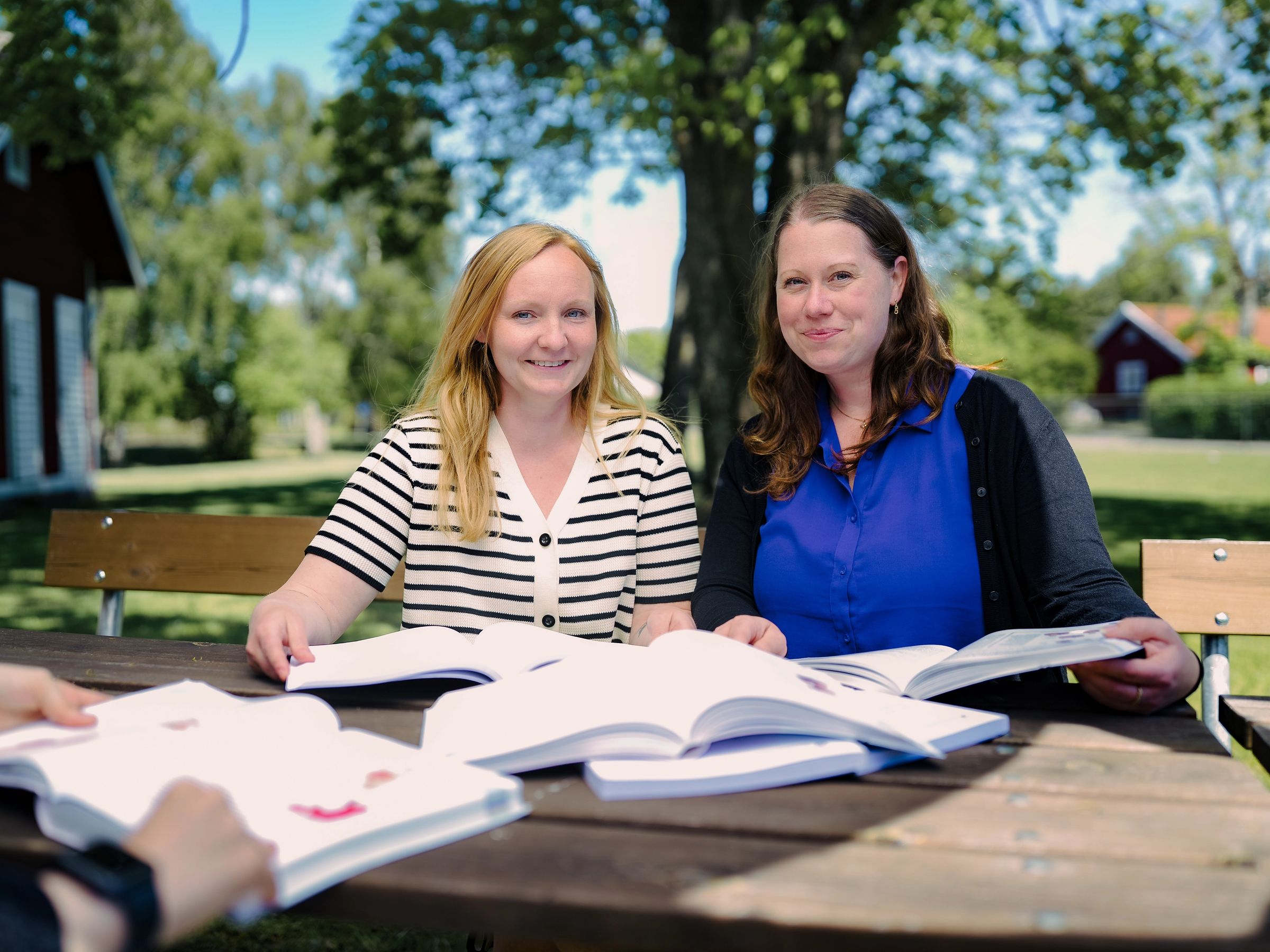 Två kvinnor sitter och läser böcker utomhus