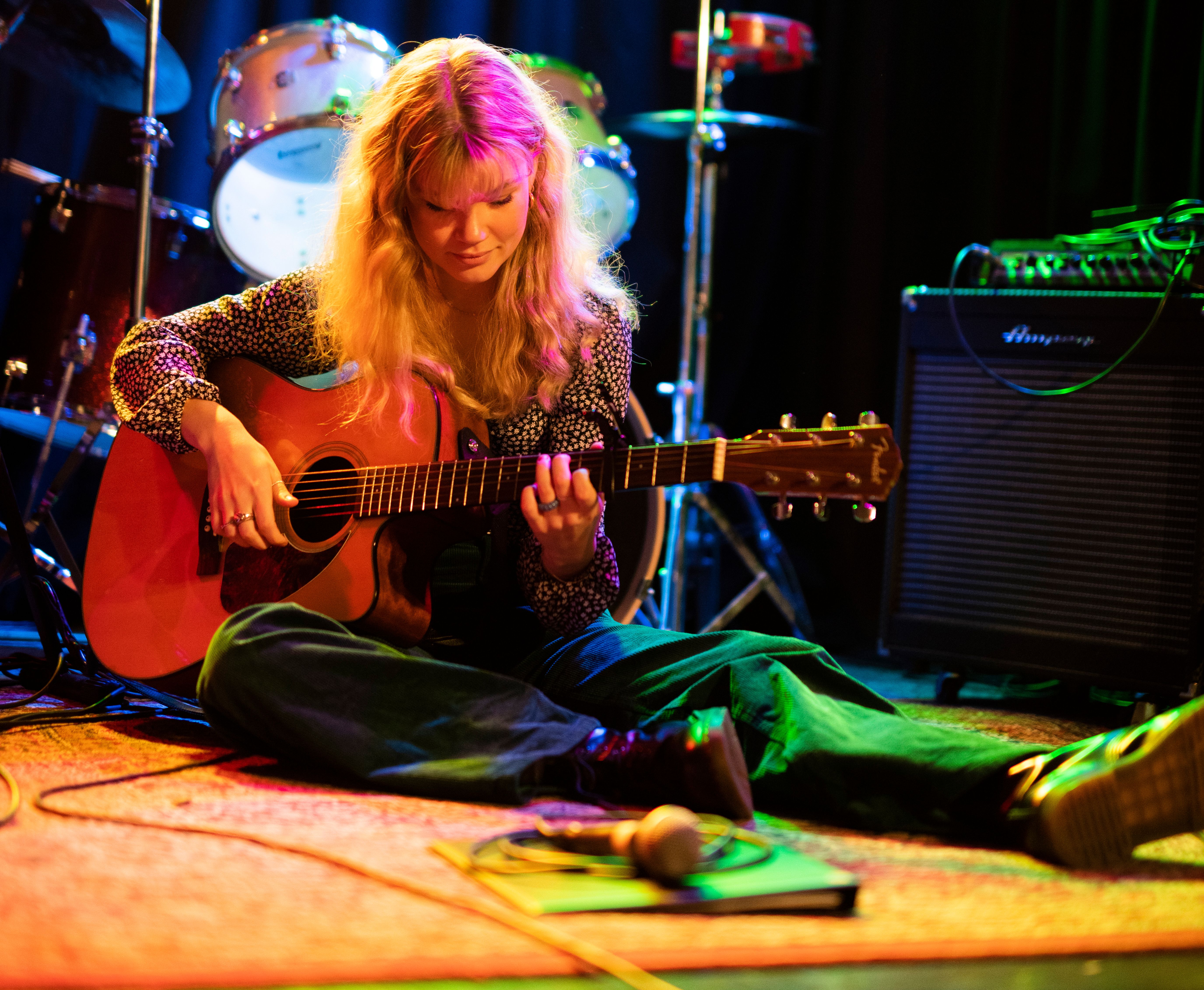 Kvinna sitter på en scen och spelar gitarr