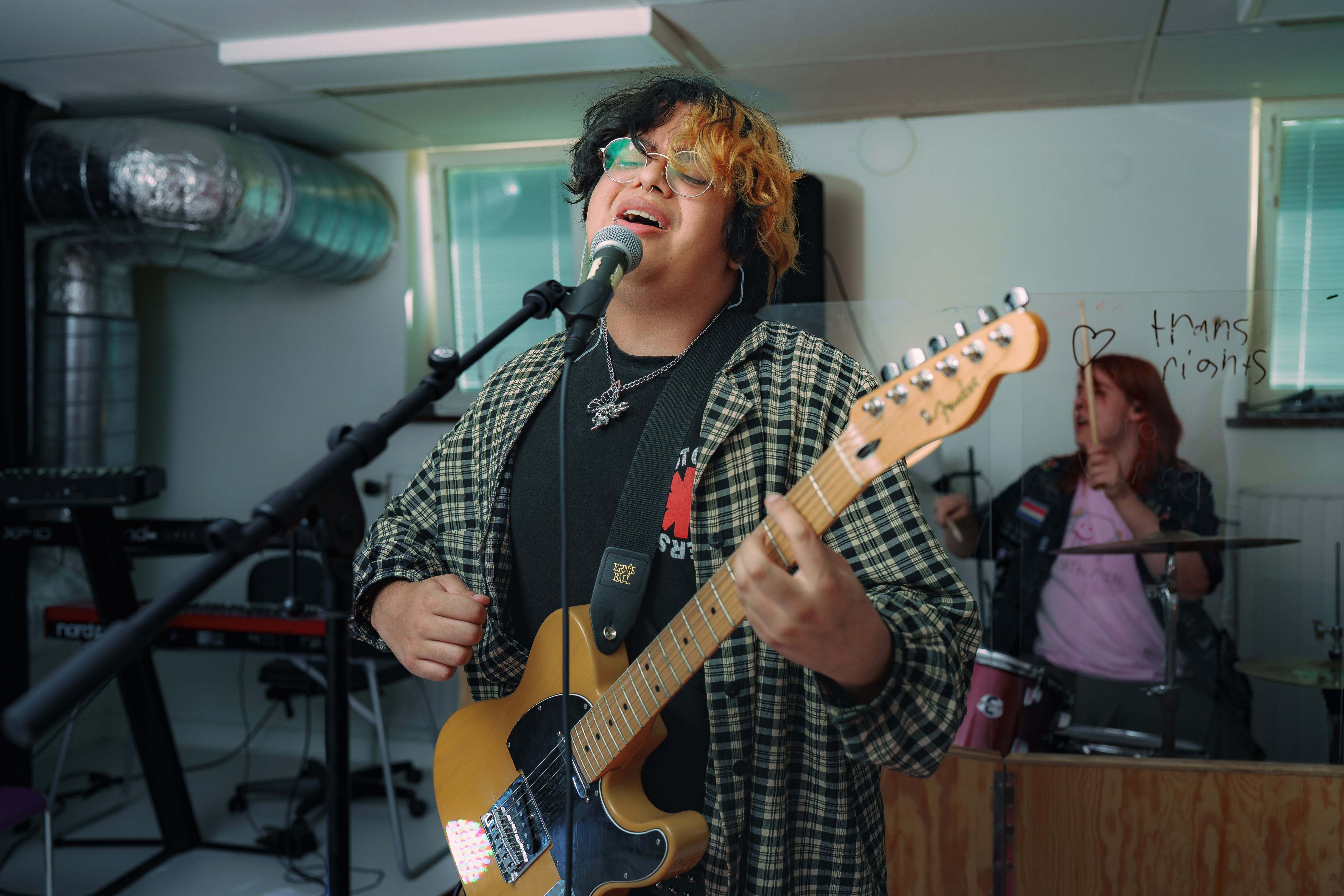 Ung man spelar på gitarr, i bakgrunden syns en trummis