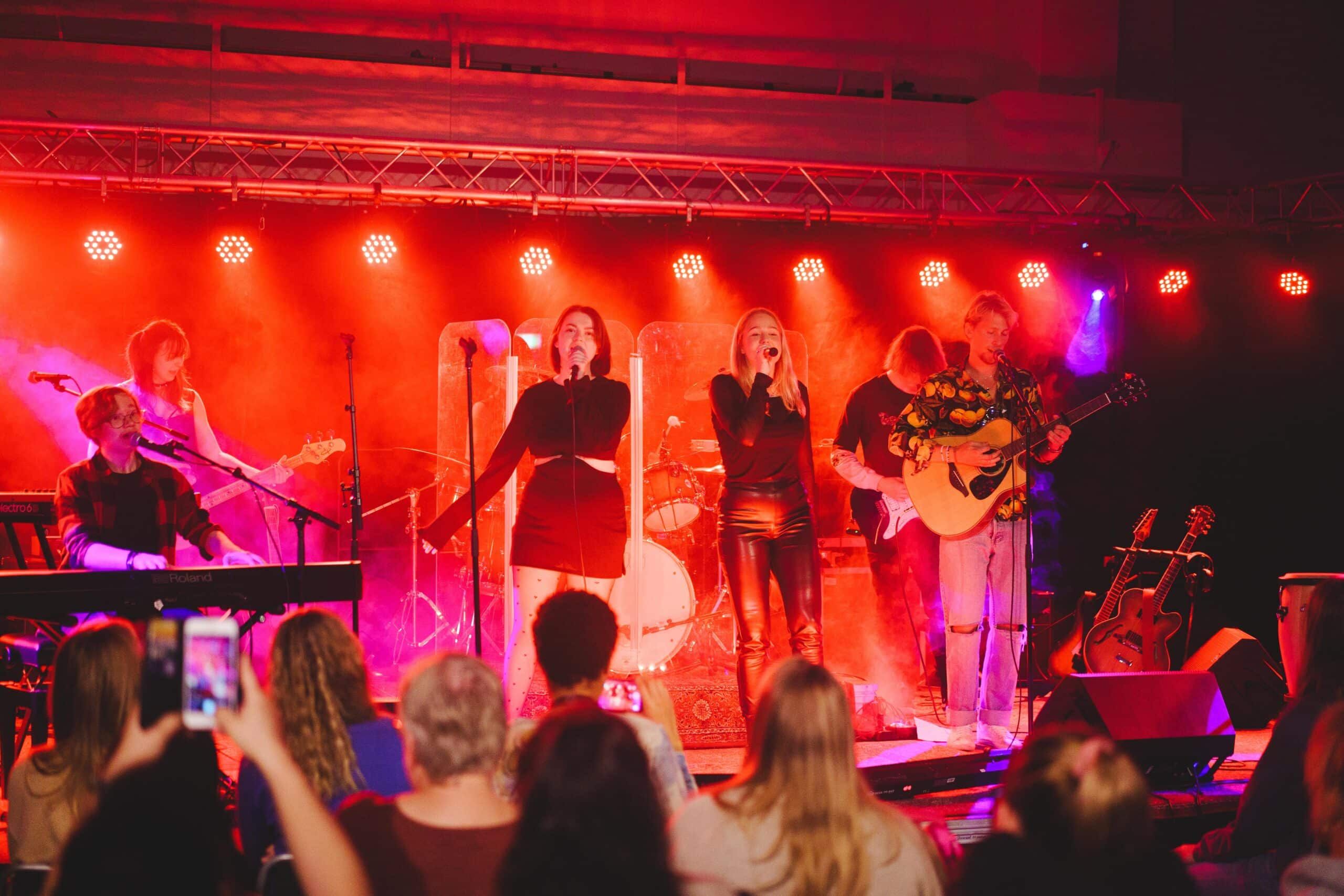 Flera personer sjunger och spelar musik på en scen framför en publik. 