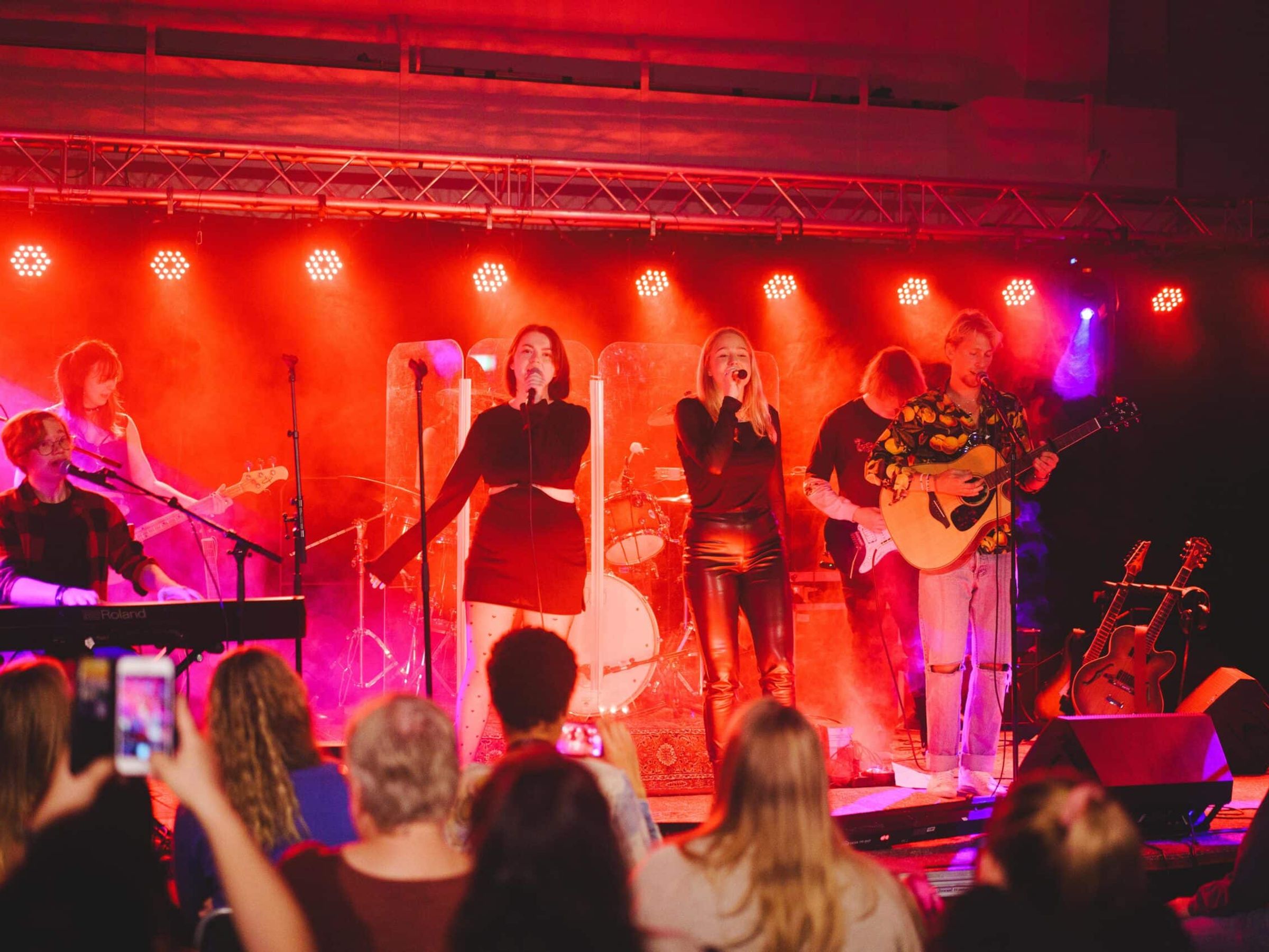 Flera personer sjunger och spelar musik på en scen framför en publik.