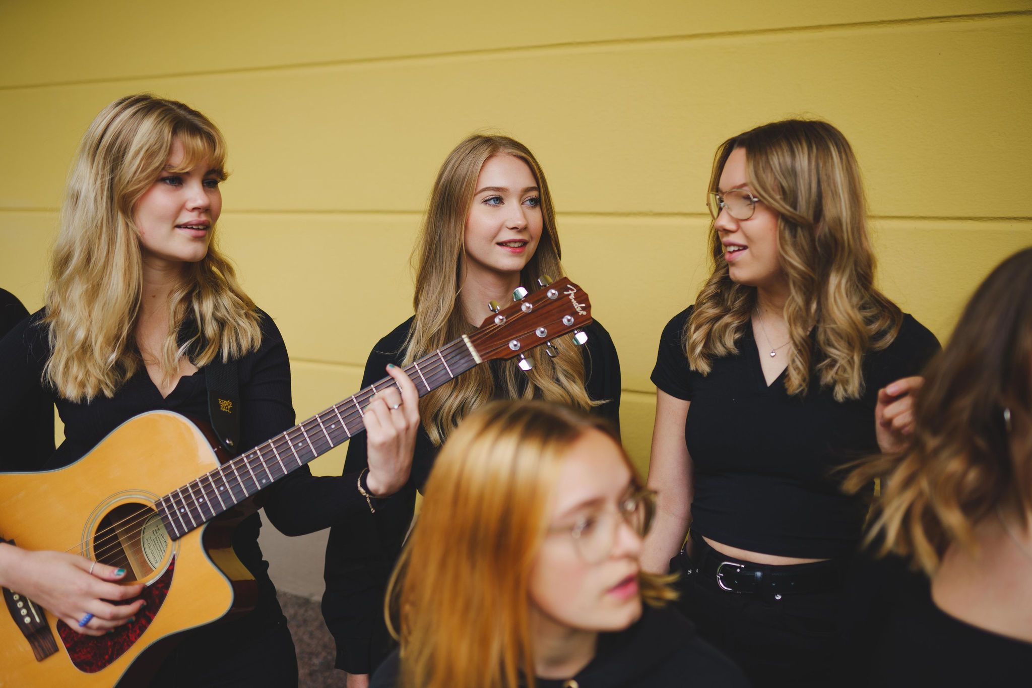 Fyra svartklädda tjejer pratar med varandra. En av dem håller i en gitarr. 