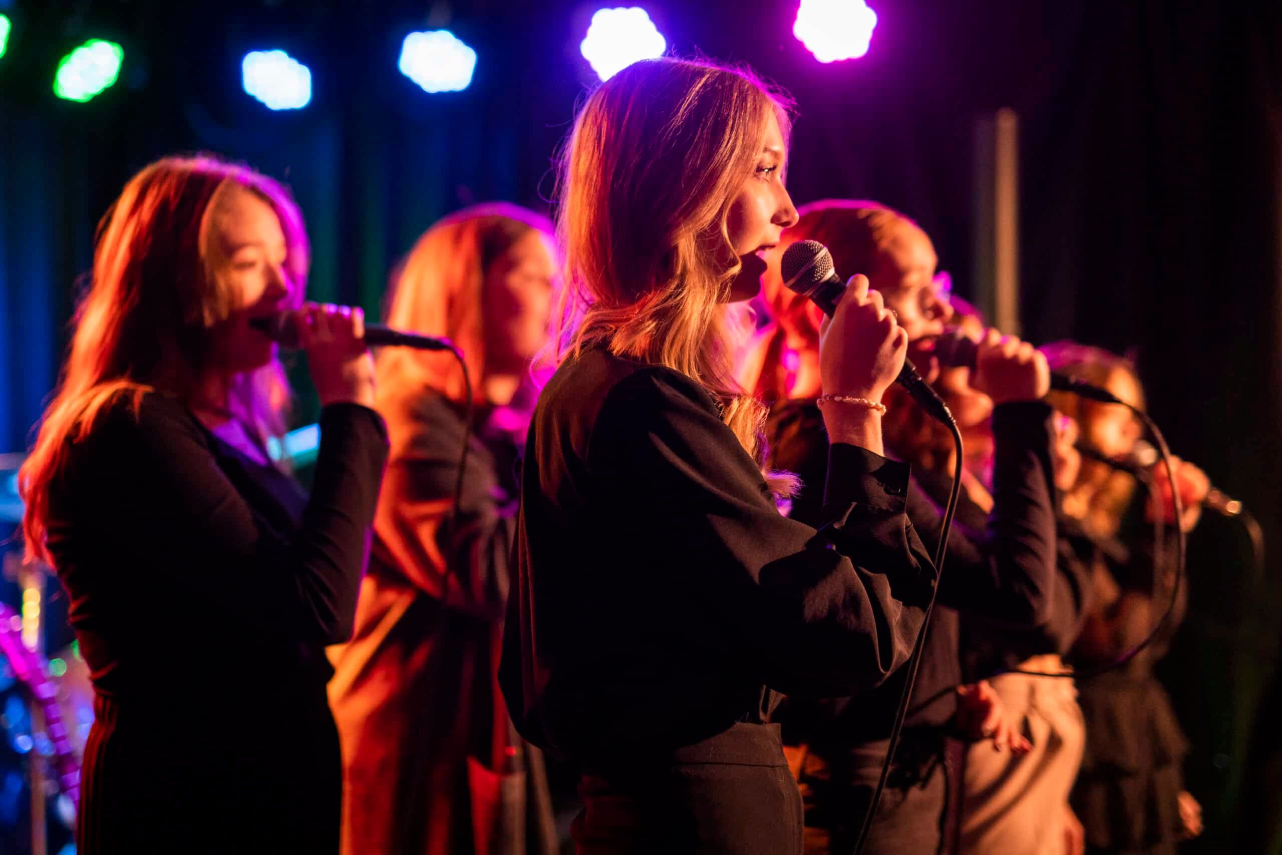 Flera tjejer sjunger tillsammans på en scen. 