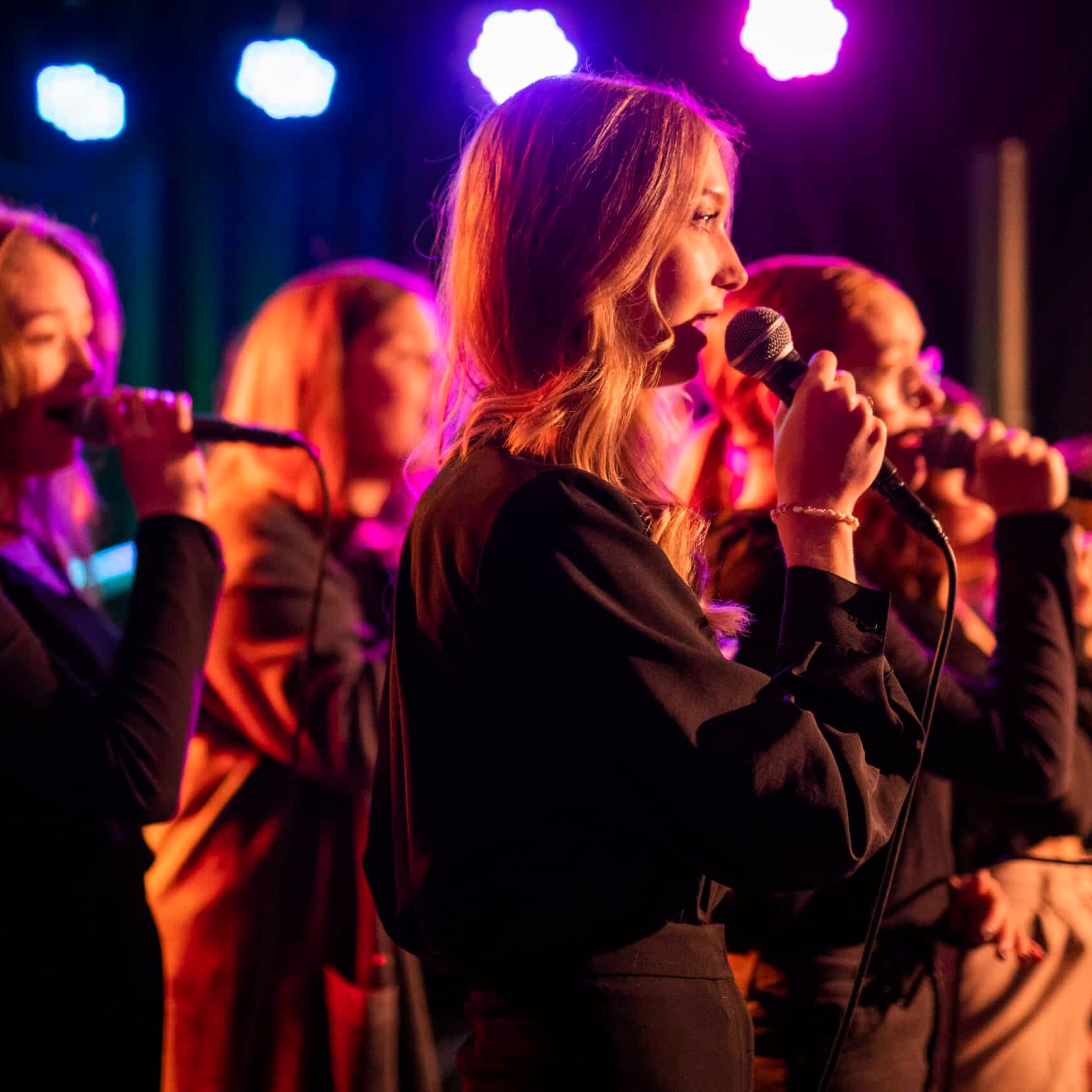 En kvinnlig kör som sjunger på en scen med fin ljussättning