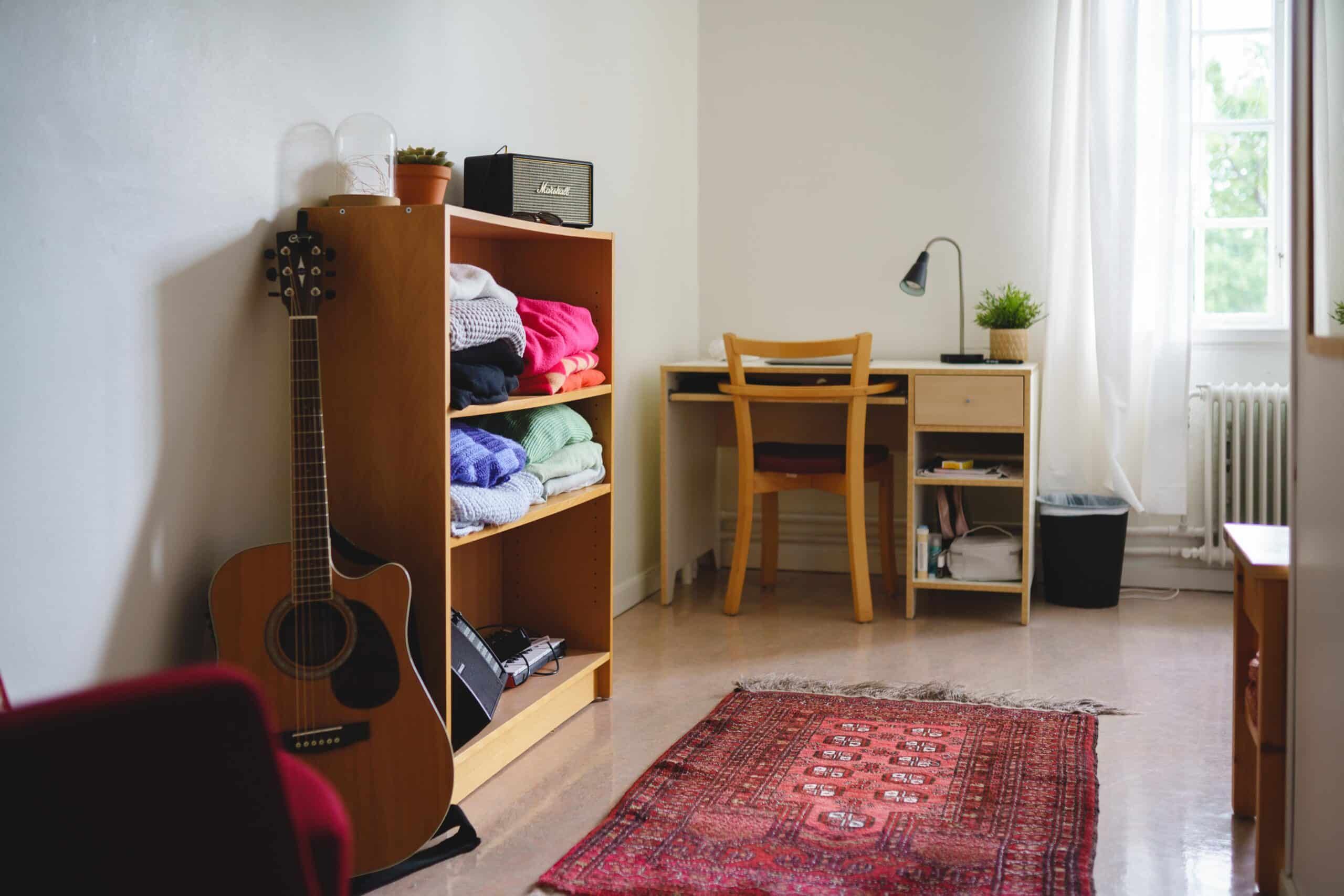 Rum på internat med röd matta bokhylla, gittar och ett skrivbord i ljus och fräsch miljö