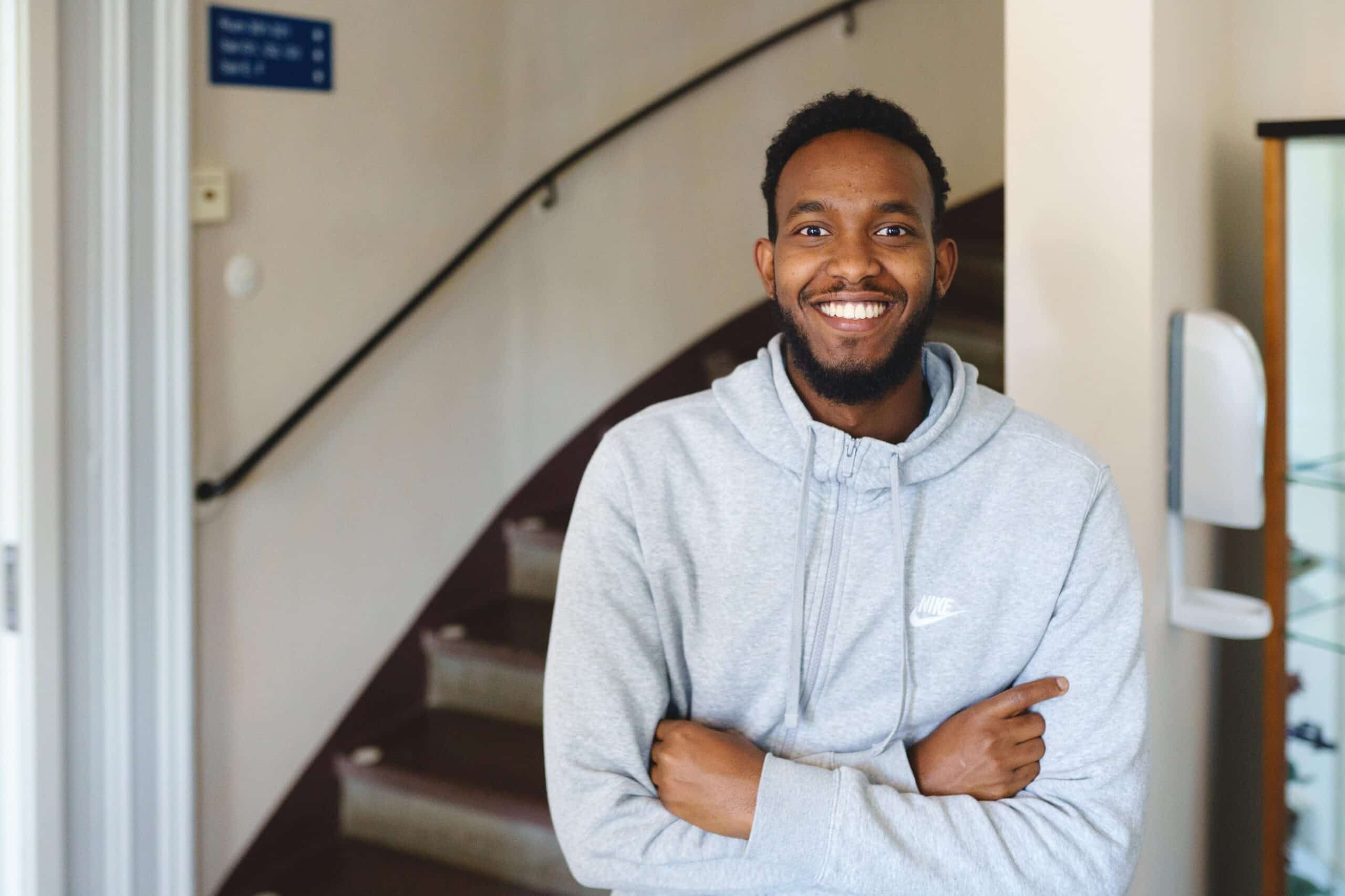 En man i grå tröja har korsade armar och ler mot kameran