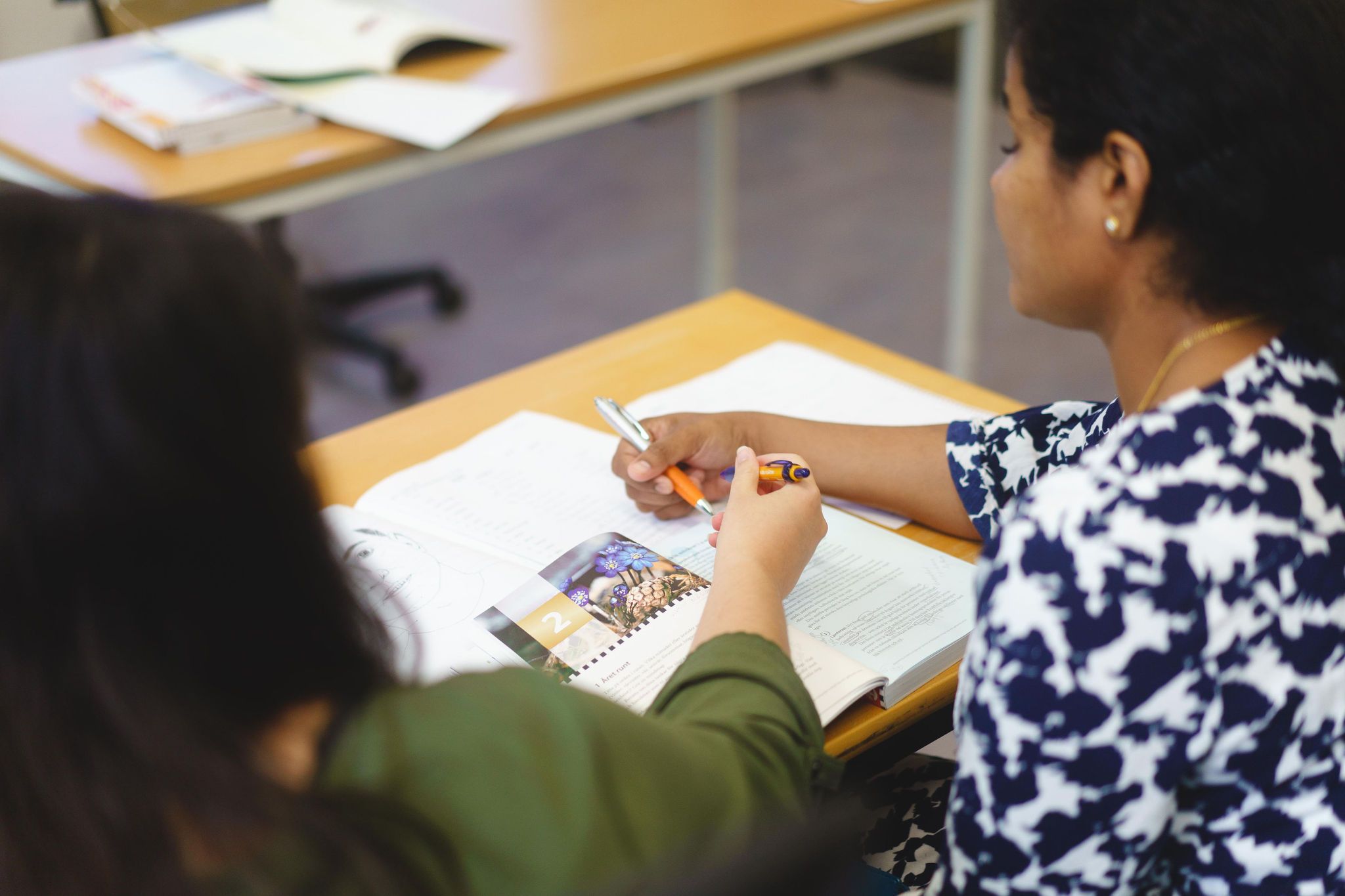 Två kvinnor studerar innehållet i en kursbok tillsammans. 