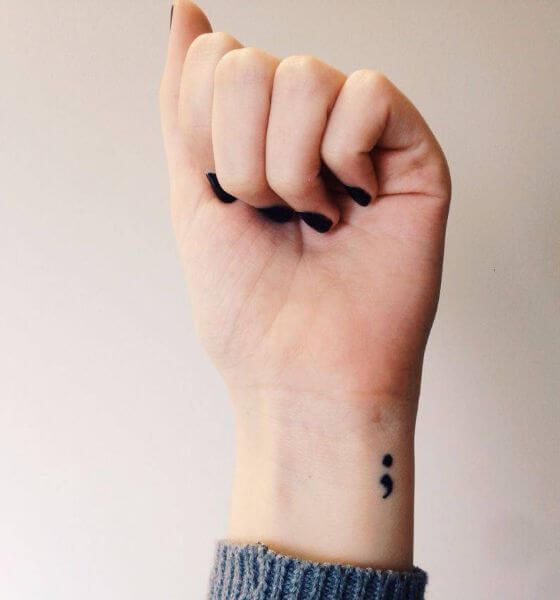 Semicolon tattoo on wrist with empowering fist pose — symbol of strength and continuation