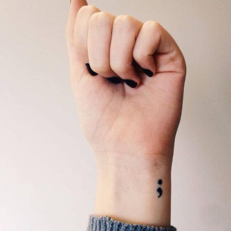 Semicolon tattoo on wrist with empowering fist pose — symbol of strength and continuation