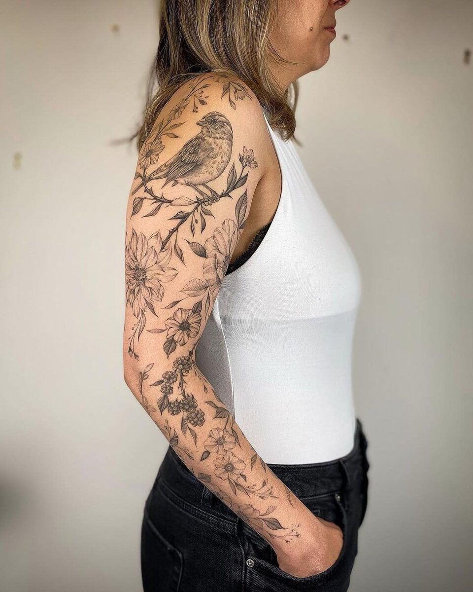 Botanical fine-line sleeve tattoo with detailed leaf and flower motifs on upper arm