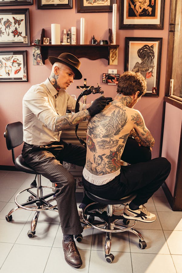 Professional tattoo artist working on a large back piece in a studio — larger tattoos cost more due to extended session time