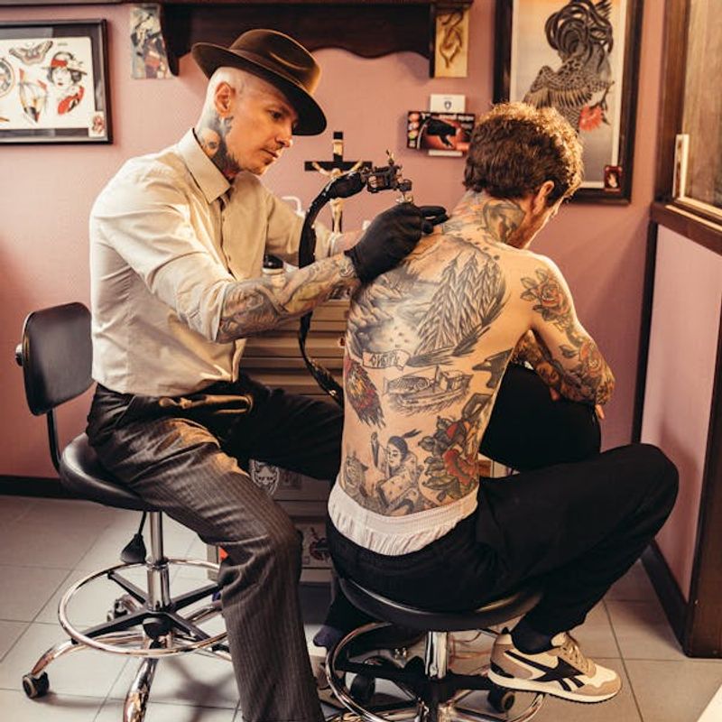 Professional tattoo artist working on a large back piece in a studio — larger tattoos cost more due to extended session time