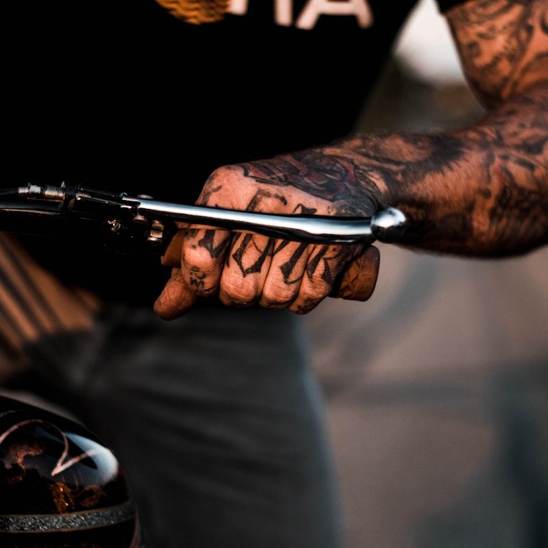 Heavily tattooed hands and arms in blackwork style holding tattoo machine