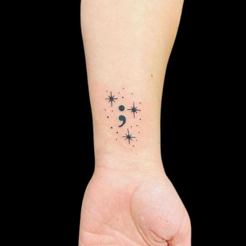 Semicolon tattoo with decorative stars on wrist — creative variation combining resilience symbolism with celestial elements
