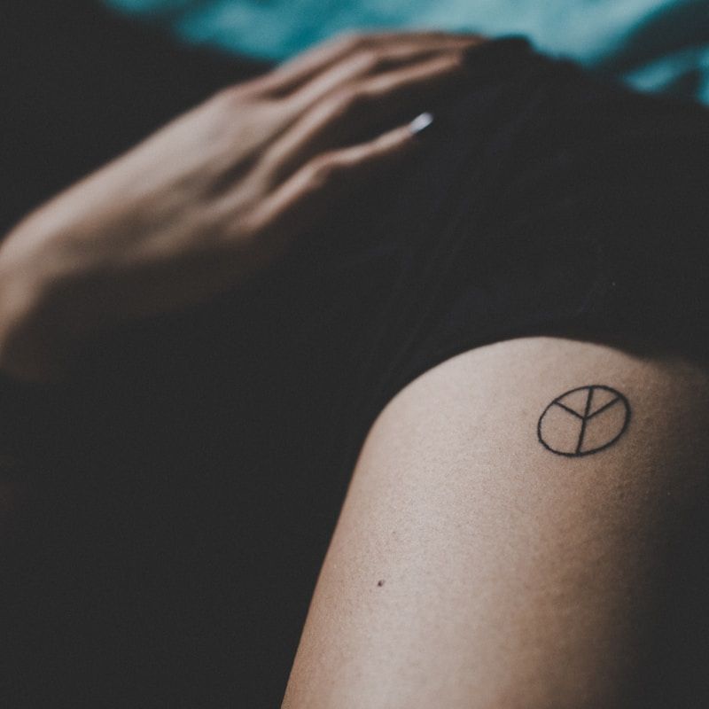Small minimalist peace symbol tattoo on shoulder