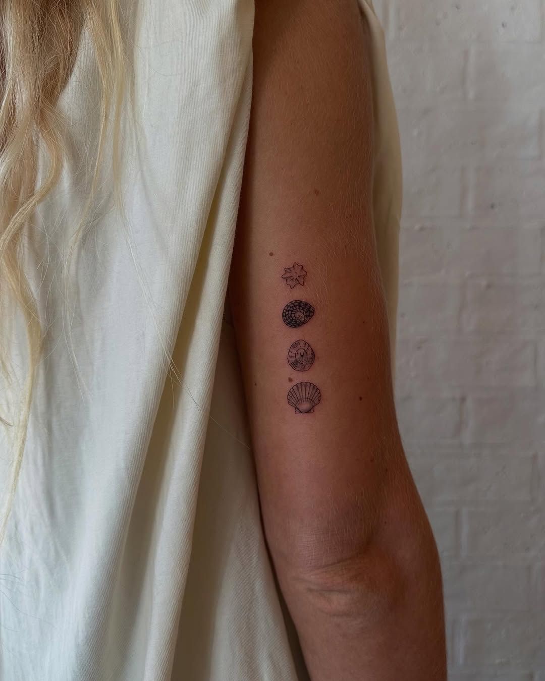 Minimalist shell and star fine line tattoo on upper arm