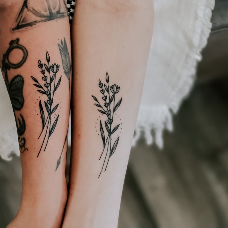 Matching minimalist wildflower bouquet tattoos on forearms