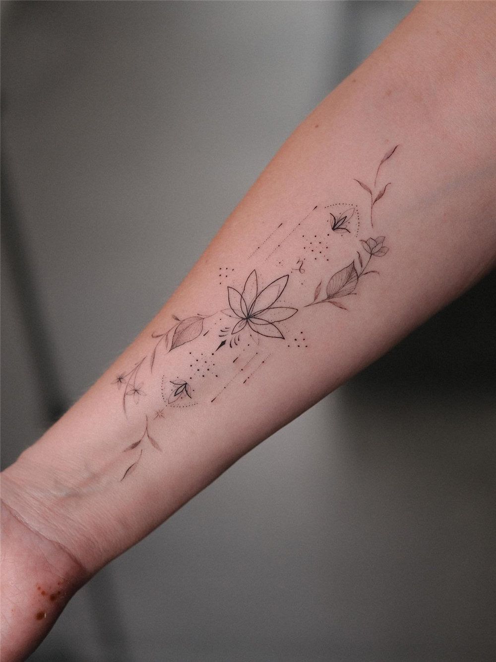 Delicate minimalist fine line tattoo with floral design on forearm