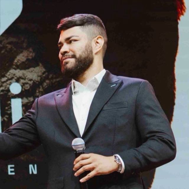 Guilherme Petersen, usando terno preto e segurando um microfone em um palco.