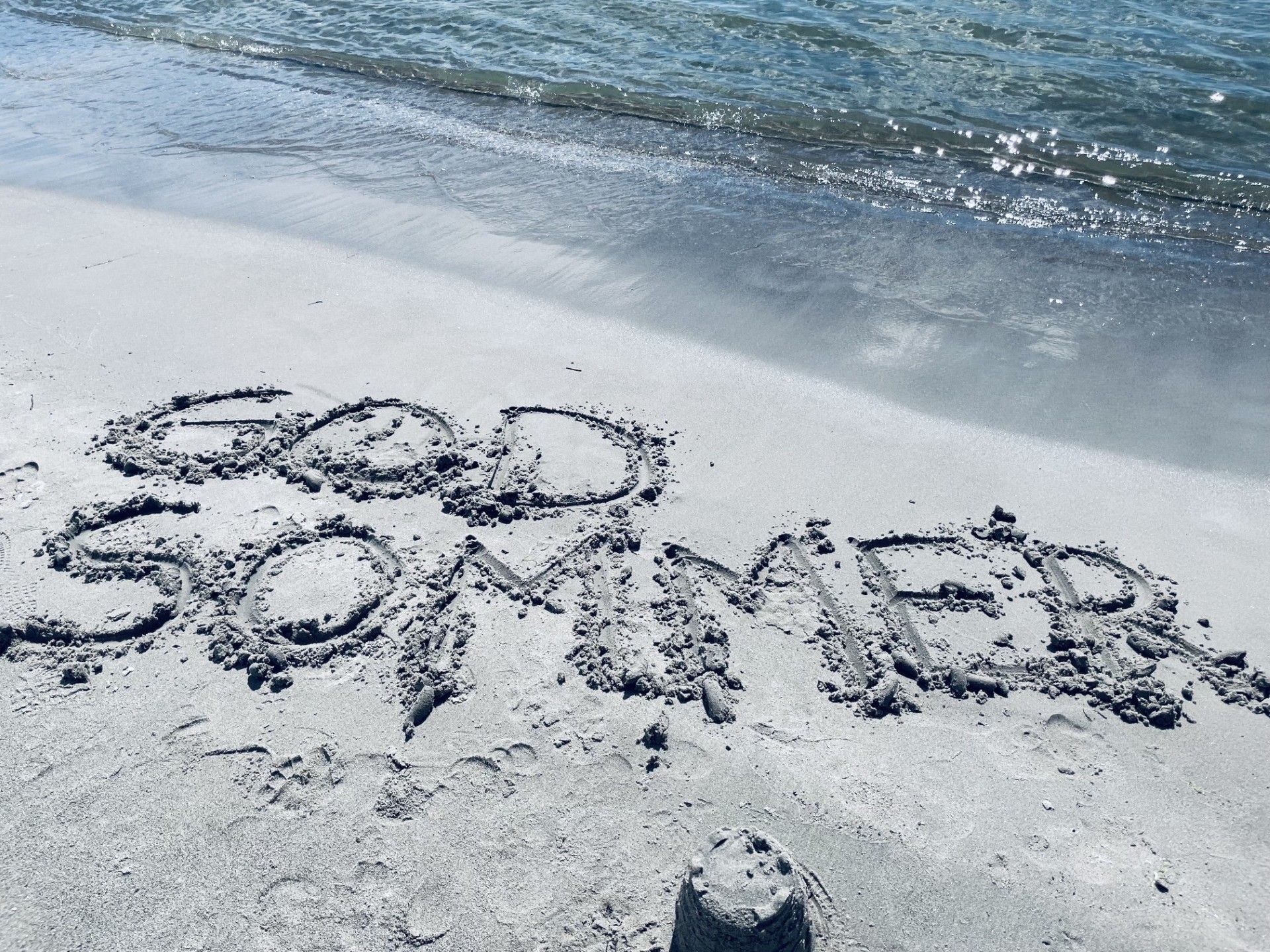 Bilde som viser teksten "god sommer" skrevet i sanden på en strand.