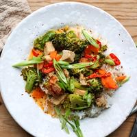 un piatto bianco contenente verdure tra cui broccoli e riso con una forchetta e un coltello neri accanto