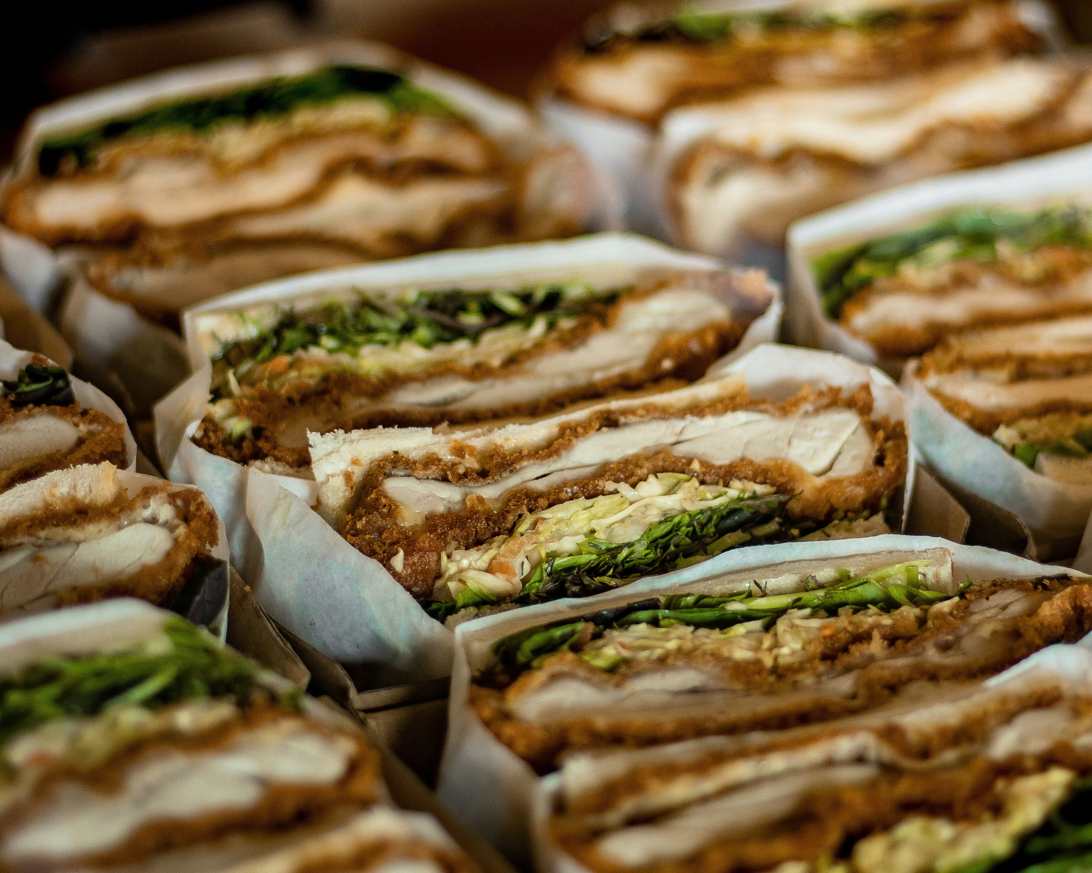 geschnittene Sandwiches mit Gemüse und Fleisch in Papier eingewickelt