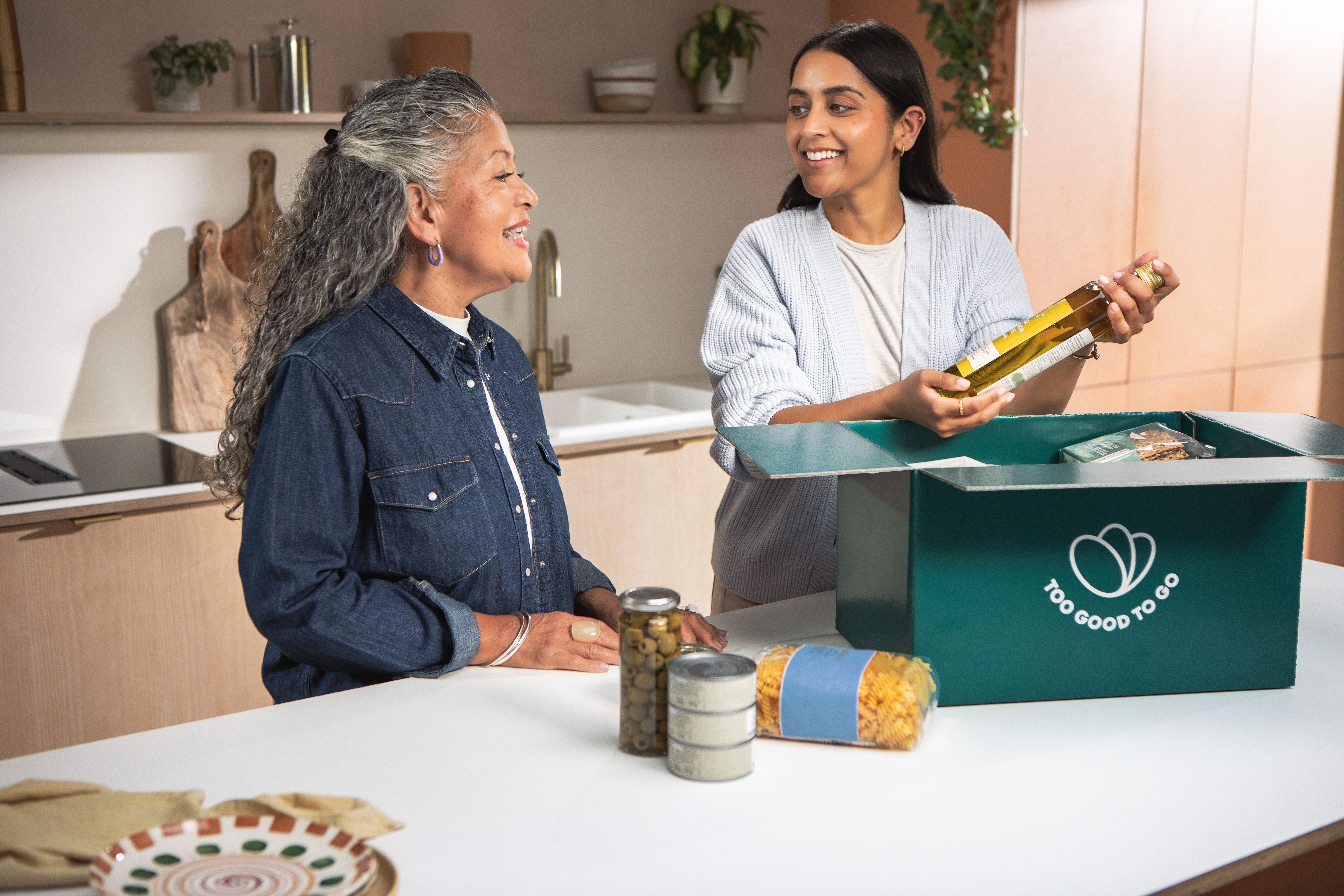 a woman is holding a bottle of olive oil next to an older woman in a kitchen .