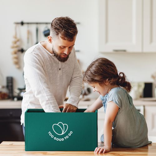 a man and a little girl are sitting at a table looking at a box .