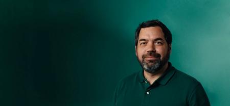 a man with a beard wearing a green polo shirt is standing in front of a green wall .