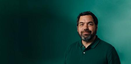 a man with a beard wearing a green polo shirt is standing in front of a green wall .