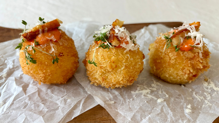 Three golden-brown crispy croquettes topped with orange sauce, grated cheese, and fresh herbs.