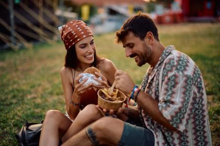 Smiling couple eating a burger and fries on grass.