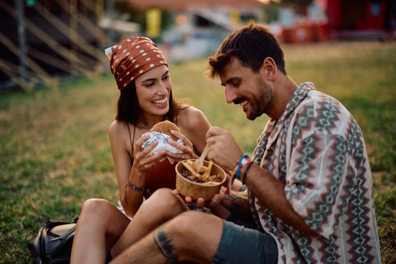 Smiling couple eating a burger and fries on grass.