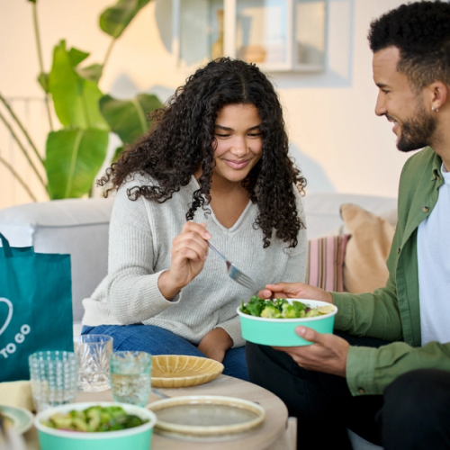 a woman is sitting on a couch eating from a green bowl