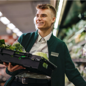 a man in a green jacket is holding a tray of vegetables