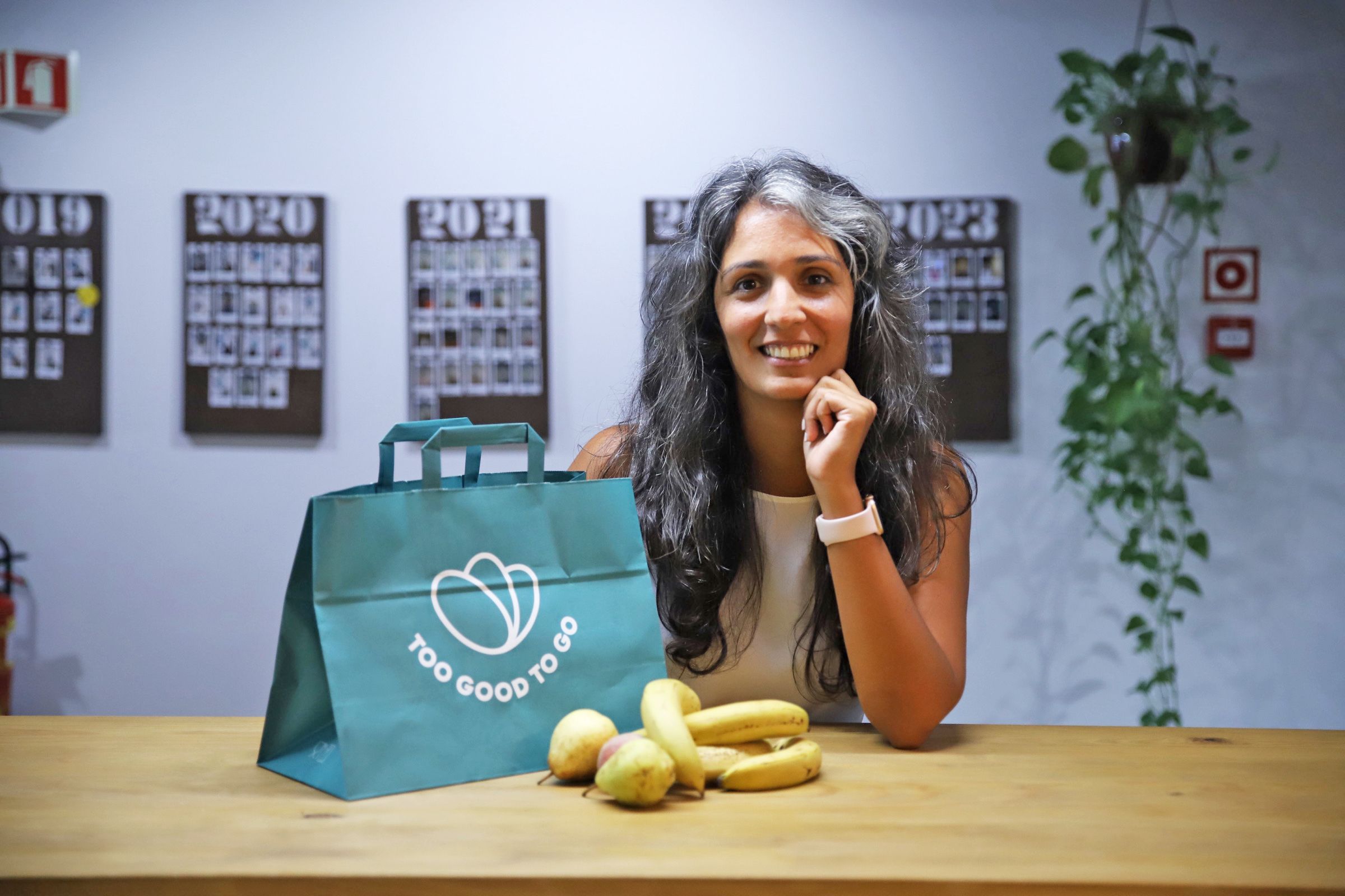 a woman is sitting at a table with a bag of bananas and pears .