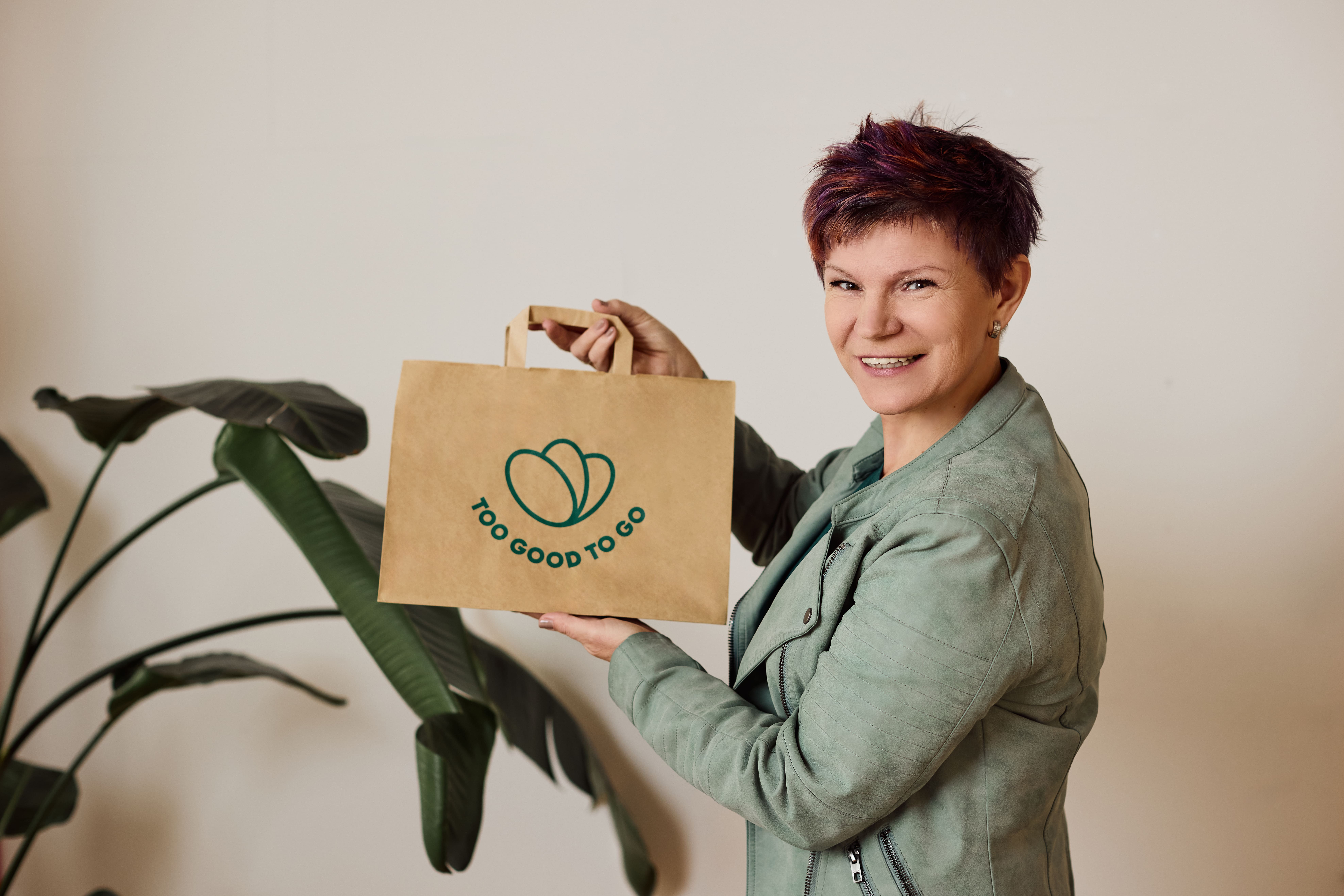 a woman in a green suit and white shirt is standing in front of a plant .
