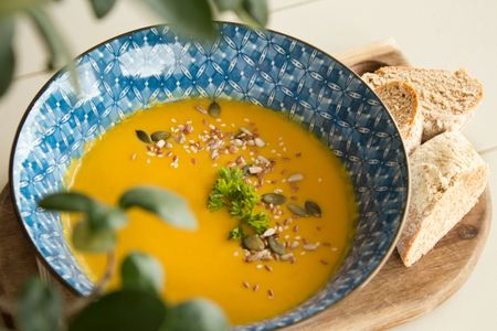 A bowl of soup with bread on a wooden cutting board.
