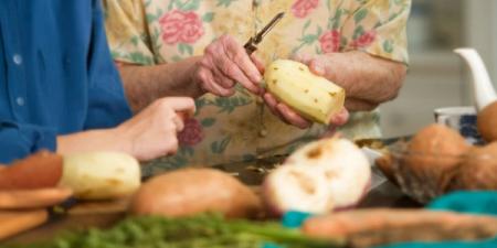 a man and a woman are peeling potatoes on a cutting board .