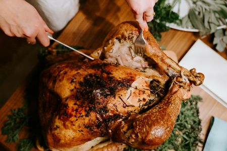 A golden-brown roasted turkey garnished with herbs is being carved on a wooden board.