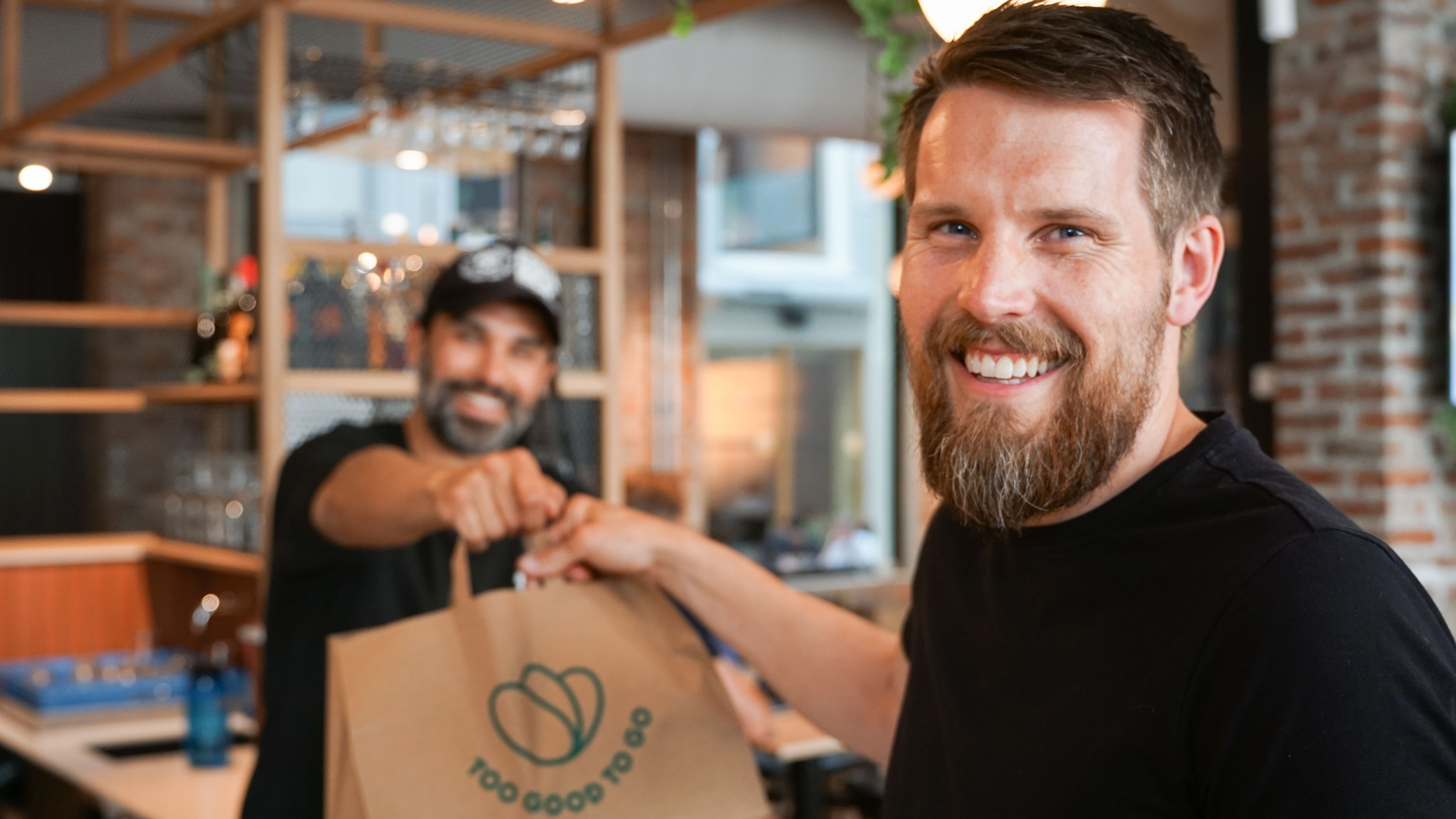 a man with a beard is giving a bag to another man in a restaurant .