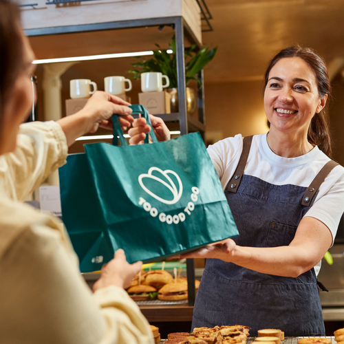 a woman holding a bag that says too good to go