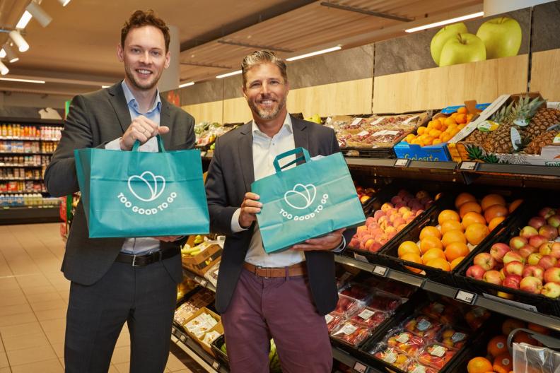 two men are holding bags in a grocery store .