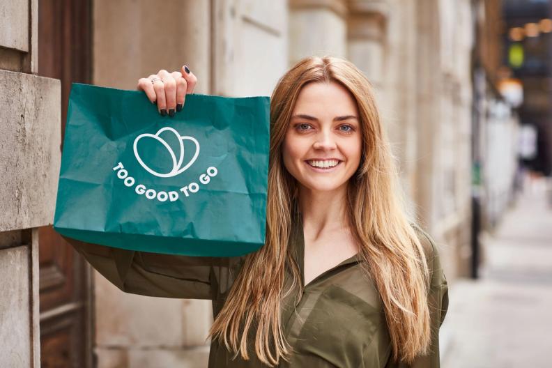 a woman is holding a green bag that says `` too good to go '' .