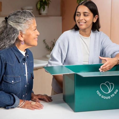 two women are sitting at a table with a box on it .