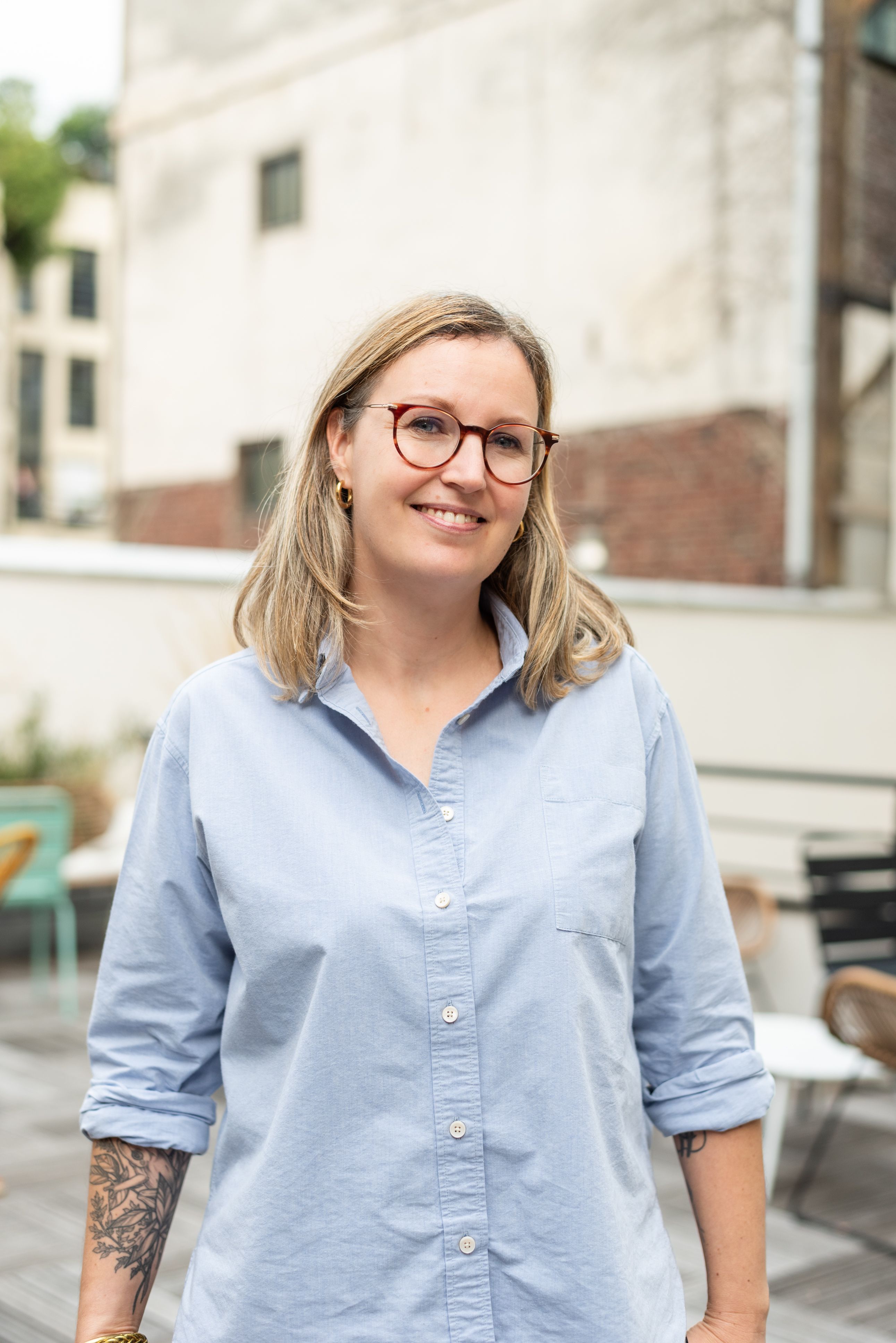 a woman wearing a black jacket and a gold necklace smiles in front of a brick wall