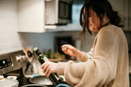 A woman is pouring olive oil into a pan in a kitchen.