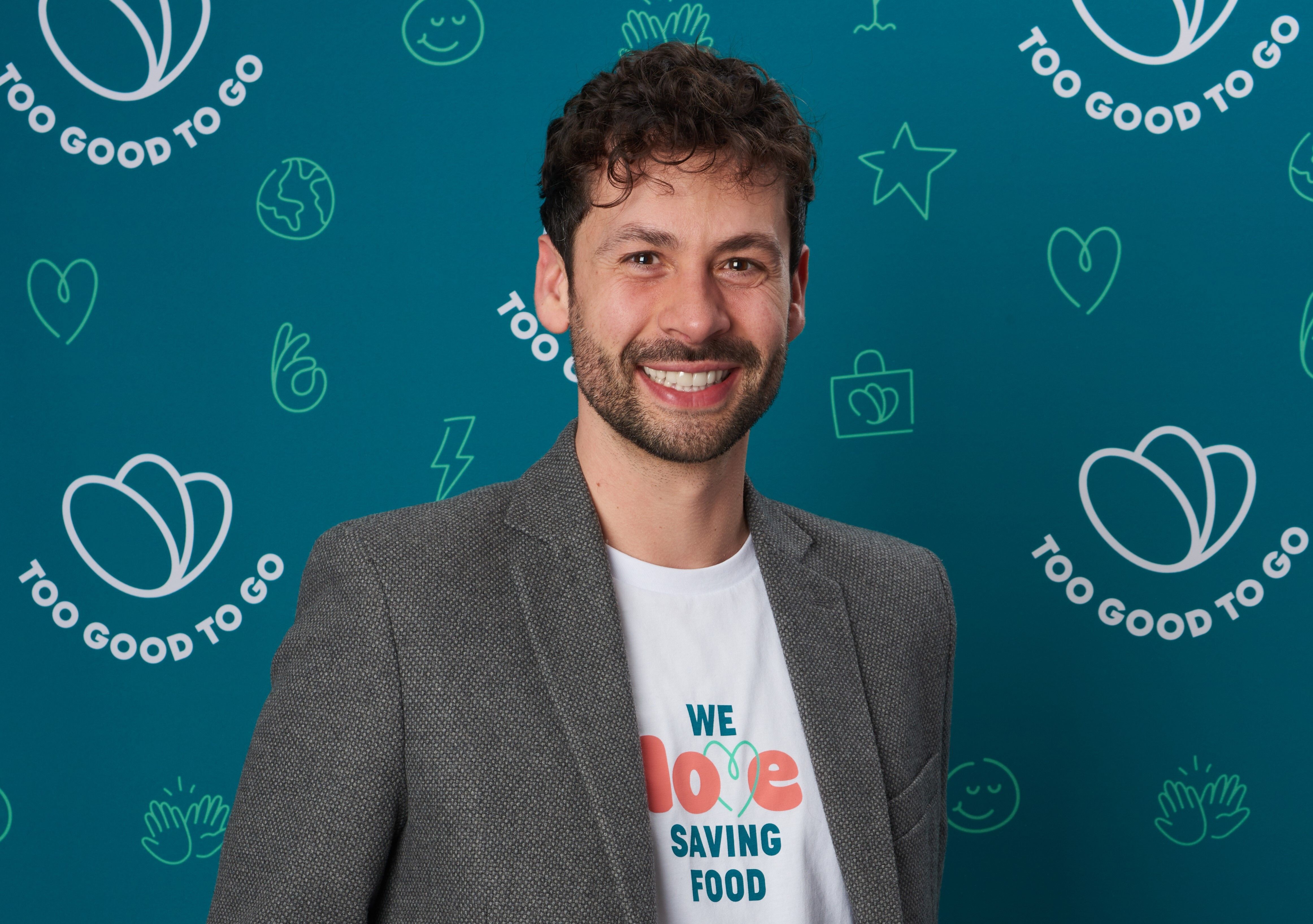 a man wearing a suit and a t-shirt that says `` we love saving food '' is smiling .